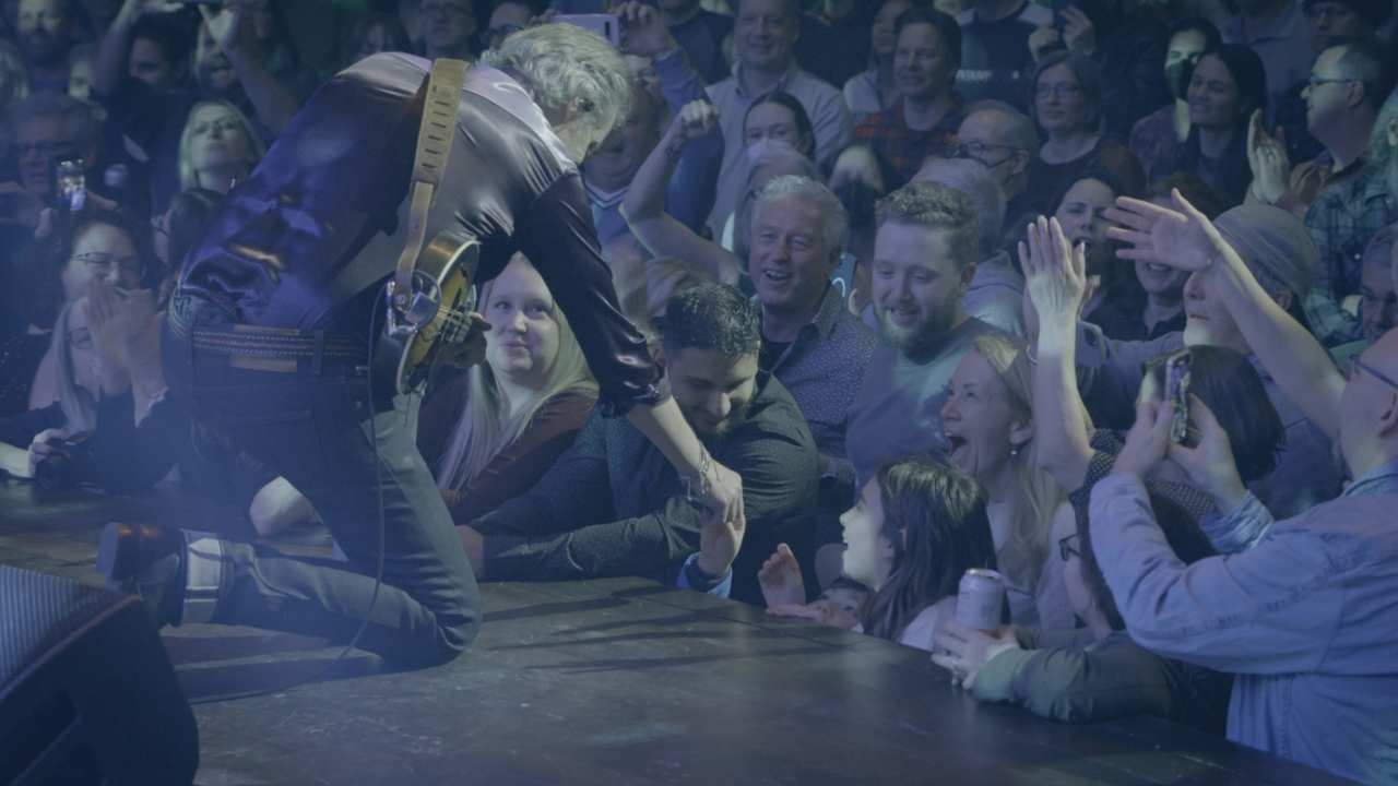 a man with a guitar on stage reaching out to fans